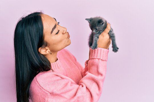 Young hispanic girl smiling happy holding cute cat over isolated pink background.