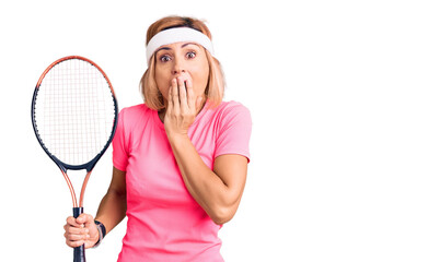 Young blonde woman playing tennis holding racket covering mouth with hand, shocked and afraid for mistake. surprised expression