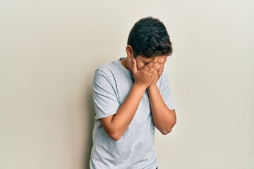 Teenager hispanic boy wearing casual grey t shirt with sad expression covering face with hands...