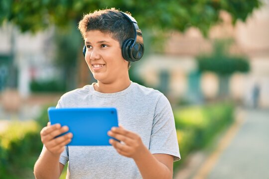 Adorable latin boy smiling happy using headphones and touchpad at the park.