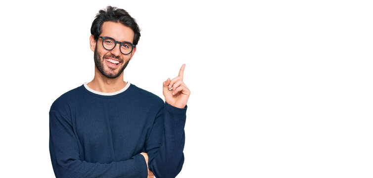 Young hispanic man wearing casual clothes and glasses with a big smile on face, pointing with hand and finger to the side looking at the camera.