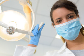 portrait of female dentist in mask adjusting the light