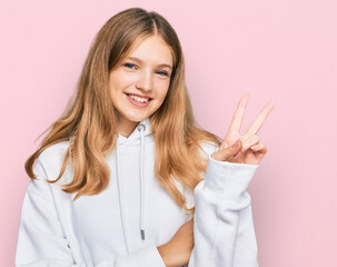 Beautiful young caucasian girl wearing casual sweatshirt smiling with happy face winking at the camera doing victory sign. number two.