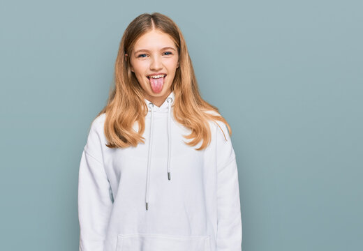 Beautiful young caucasian girl wearing casual sweatshirt sticking tongue out happy with funny expression. emotion concept.