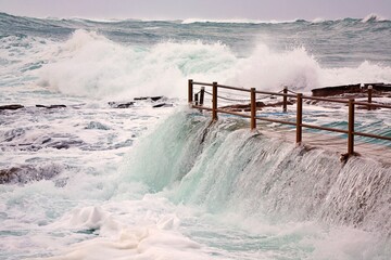 Overflowing flooded ocean rock pool during storm with crashing rough waves in the background