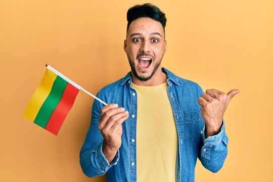Young arab man holding lithuania flag pointing thumb up to the side smiling happy with open mouth