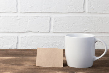 Household utensils, a white cup stands on a shelf on a wooden table against the background of a kitchen stone brick wall of a milky shade, the concept of clean dishes