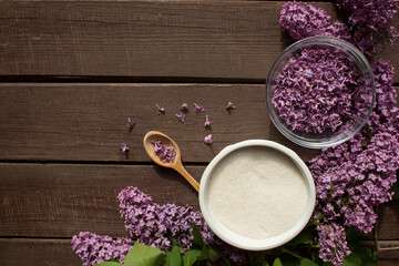 Everything prepared for homemade lilac sugar - Purple lilac flower, wooden spoon, sugar in white bowl on dark wooden background with bunch of fresh flowers, 