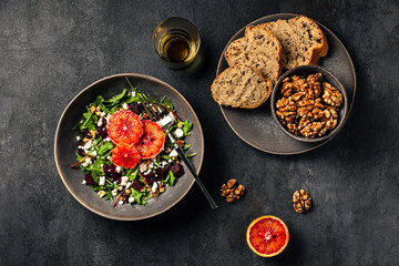 Salad with rocket, chard, beetroot, feta or brynza cheese, walnuts and blood orange. Bread and walnuts, a glass of white wine. Top view photo.