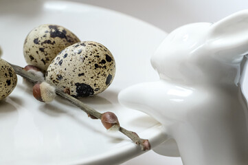 Cute white ceramic rabbit tries to reach for spotted egg with its paw. Happy easter holiday concept