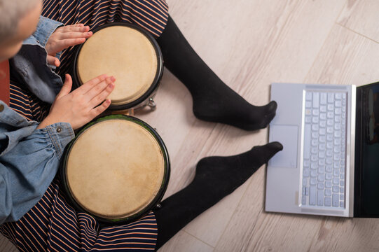 A faceless woman sits on the floor at home and watches educational videos of playing mini bongs. Girl remotely learns to play traditional ethnic drums.