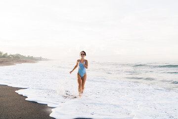 Fototapeta na wymiar Attractive woman in swimwear running on wet seashore