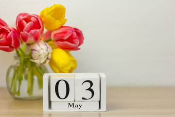 May 1 on a wooden calendar next to a bouquet of tulips.One day of the spring month.
