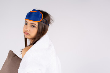 Concept of healthy sleep. Sleepy girl yawning, exhausted, wrapped in blanket and with eyemask on her head isolated on grey background with side empty space