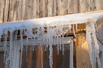 Spring ice icicles on roof of greenhouse. Patterns scattered by sun and frost