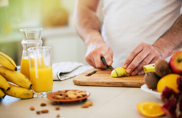 Handsome young sporty smiling man in the kitchen is preparing vegan healthy fruits salad and smoothie in a good mood