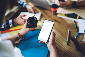 Cropped female connecting to 4g internet for browsing media app on mockup mobile gadget with copy space area for web advertising, unrecognizable blogger with coffee to go networking on blank cellphone