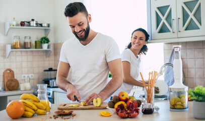 Excited happy beautiful young couple in love cooking in the kitchen and having fun together while making fresh healthy fruits salad