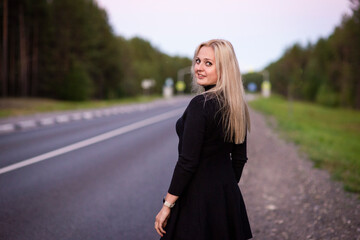 Fototapeta na wymiar blonde girl in black dress on the road, selective focus