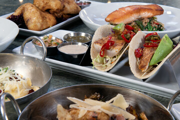 Full table of a variety of restaurant dishes to choose from with pan roasted fish tacos in the center.