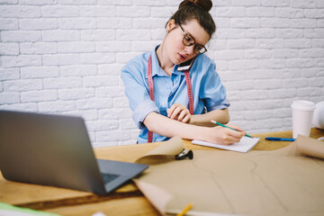 Focused tailor speaking on mobile phone and taking notes in notebook