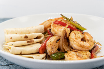 Jumbo pieces of fajita style shrimp piled on stir fry vegetables combined with folded tortillas to eat as a delicious meal.