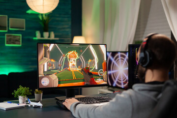 Back view shot of focused pro gamer streaming videogames on professional computer using headphones. Online streamer cyber performing during gaming tournament using technology network wireless © DC Studio