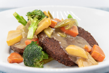 Meatless vegan patty drizzled with gravey and covered with chopped broccoli, carrots, and other mixed vegetables for a delicious vegetatian meal.