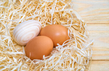 Two  eggs and wooden egg in a nest with wood shavings. Idea for celebrating Easter