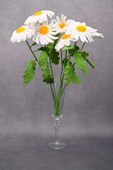 A bouquet of daisies knitted from soft yarn. The bouquet is in a glass wine glass.