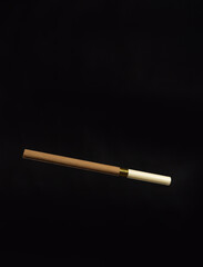 An unlit brown cigarette with a beige mouthpiece on a dark background.