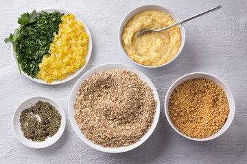 Ingredients for vegan nut cutlets with vegetables and greens, ground nuts, bread crumbs, blended potatoess, fried onions, chopped parsley and spices on a light gray background