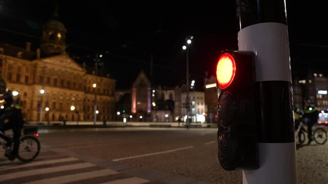 Municipality enforcers walk and cycle through empty streets in Amsterdam during Covid-19 evening curfew (focus on red traffic light).
