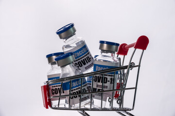 Glass vials for Covid-19 vaccine in shopping cart on white background. Group of Coronavirus vaccine bottles in basket.