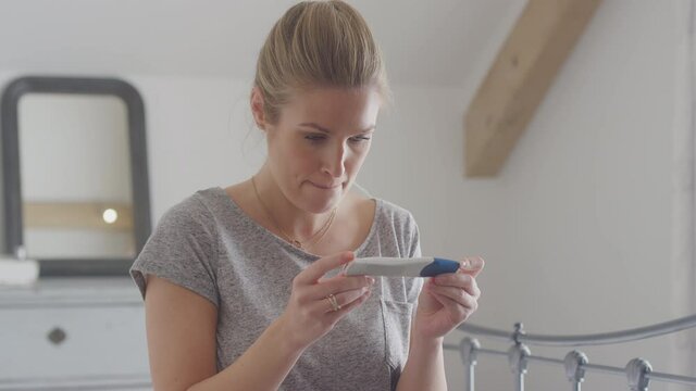 Disappointed young woman wearing pyjamas sitting on bed at home looking unhappy after negative result from home pregnancy test - shot in slow motion