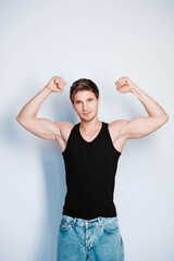 Muscular young man shows biceps in black t-shirt on a white background. Copy, empty space for text