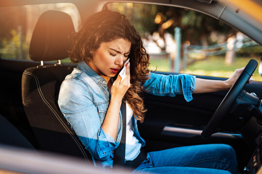 Young woman sneezing while driving car. Healthcare, virus, allergy concept.