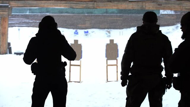 A man and a woman shoot pistols at a shooting range in winter, a view through the backs on a target. silhouette, medium shot, full HD, no sound.