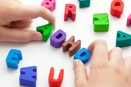 A young boy holding the abbreviation ADHD that is made out of polymer clay letters. ADHD is Attention deficit hyperactivity disorder.