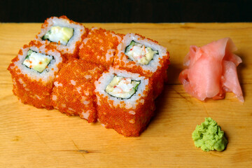 rolls of meat crab soft cheese cucumber red caviar ginger wasabi served on a wooden stand on a dark background