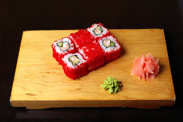 rolls of shrimp cucumber soft cheese red caviar ginger wasabi served on a wooden stand on a dark background