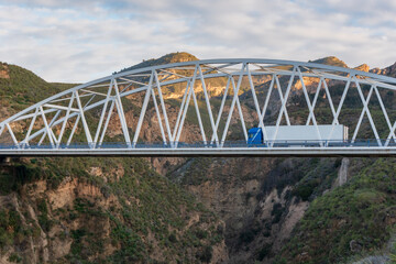 Truck with refrigerated semi-trailer on an iron bridge connecting two mountains.