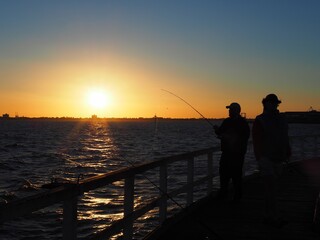 Fototapeta premium People fishing at the Pier and sun is setting in the backdrop . Location Lagoon Pier in Port Melbourne, Victoria , Australia