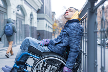 Young man in the wheelchair looking up and leaning on barrier. Side view