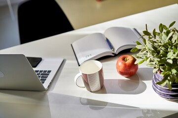 Laptop and cup of coffee or tea on desk at home. Cosy study room in morning lights.