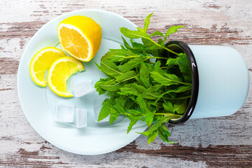 Lemon and ice cubes on blue plate, mint leaves in mug on wooden background