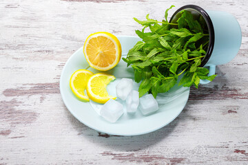 Mint leaves in mug, lemon and ice cubes on blue plate on wooden background