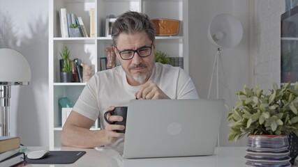 Older man working online with laptop computer at home sitting at desk. Home office, browsing internet, study room.