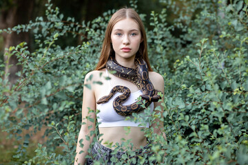 Young girl holding a snake around her neck and standing near the bush