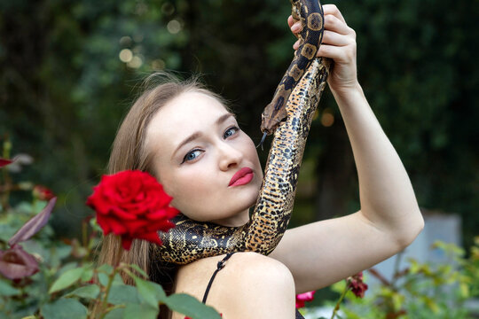 Woman holding a snake in hand and looking at camera in roses